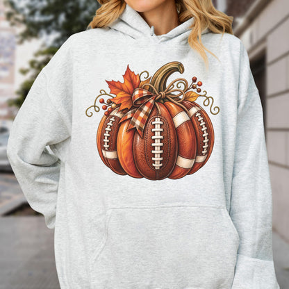 May include: A light gray hooded sweatshirt featuring a central graphic of a pumpkin designed with the texture and white laces of an American football. The pumpkin is decorated with a plaid ribbon bow, an orange maple leaf, and brown berries.
