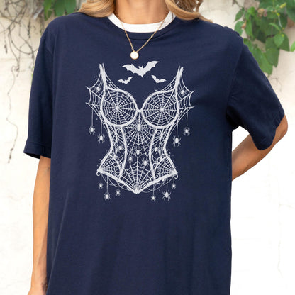 May include: A navy blue short-sleeve t-shirt featuring a white graphic print of a corset made from spiderwebs. The design includes several small spiders hanging from the webbed corset and three bats flying above the neckline of the corset graphic.