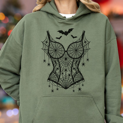 May include: An olive green hooded sweatshirt featuring a black graphic print of a corset design made of spiderwebs and spiders. The design includes three black bats flying above the corset, with multiple small spiders hanging from the webbed fabric.