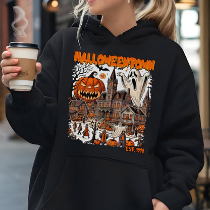 May include: A black hooded sweatshirt featuring a graphic print with the text HALLOWEENTOWN EST. 1998. The design depicts a spooky town scene with a large jack-o'-lantern, a tall clock tower, ghosts, and various figures in an orange and black color palette.