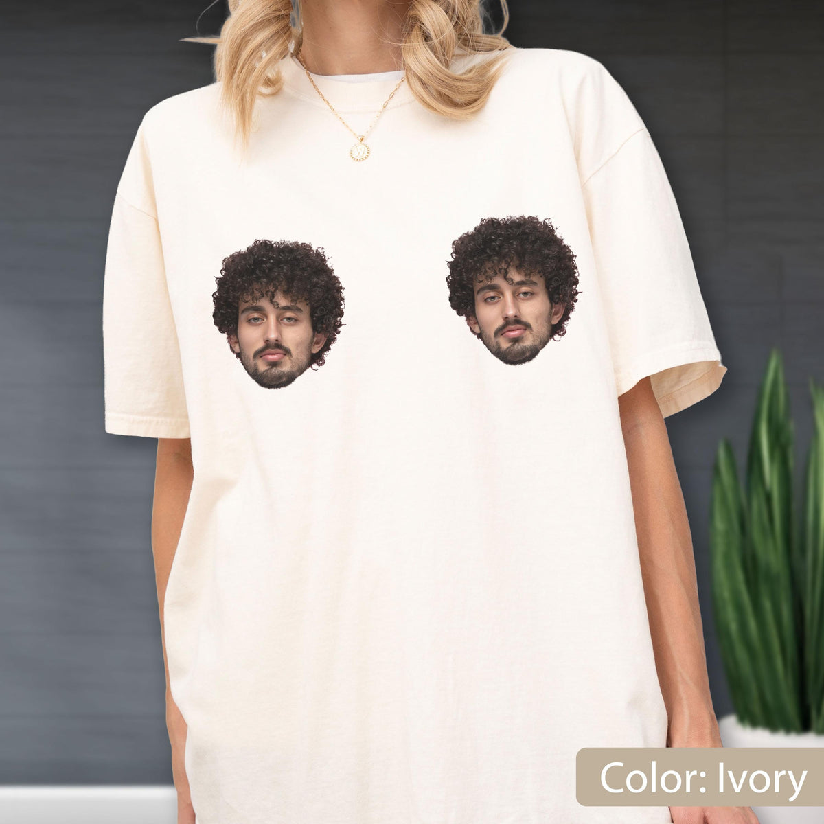 May include: An ivory short-sleeved t-shirt featuring two identical photographic prints of a person with dark curly hair and a beard. The graphic is positioned on the upper chest area of the garment, which has a crew neckline and a relaxed fit.