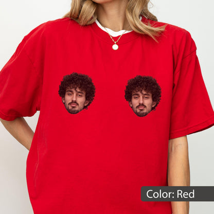 May include: A bright red short-sleeved t-shirt featuring two identical graphic prints of a person with dark curly hair and a beard positioned on the chest area. The shirt has a crew neckline and is worn with a simple gold chain necklace.