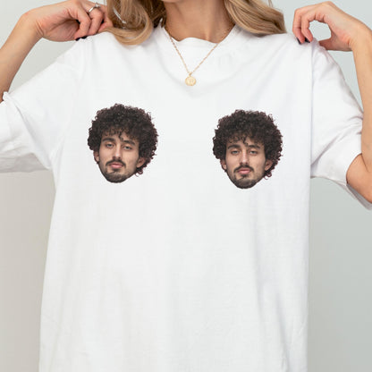 May include: A white short-sleeved t-shirt featuring two identical photographic prints of a person with dark curly hair and a beard. The images are positioned on the chest area of the garment, which has a crew neckline and a relaxed fit.