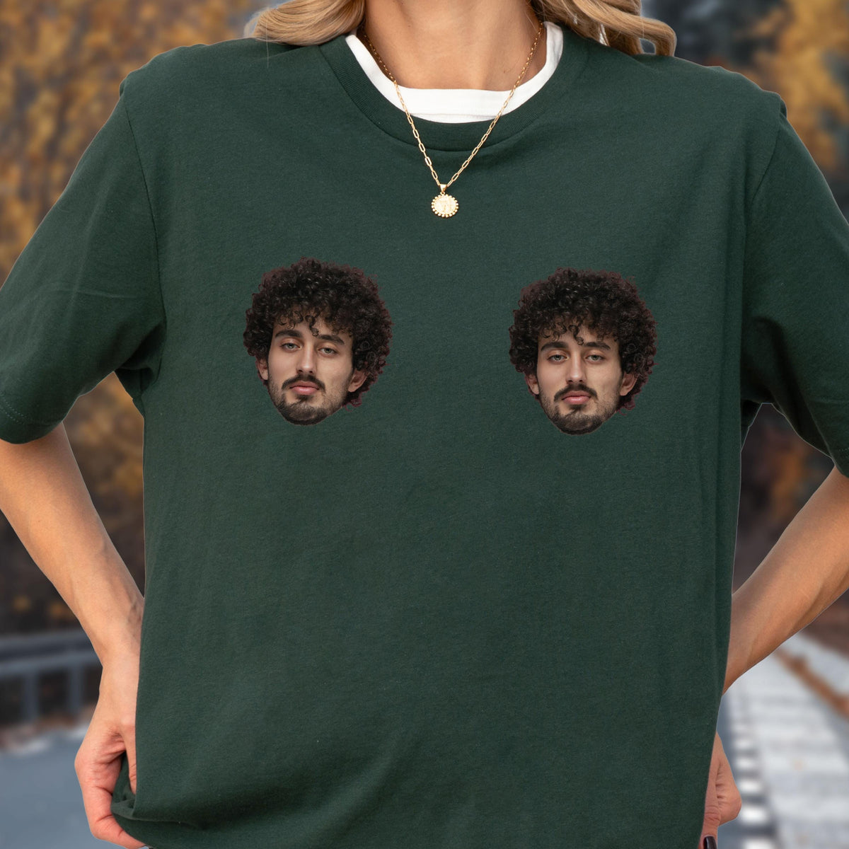 May include: A dark forest green short-sleeved t-shirt featuring two identical photographic prints of a person with dark curly hair and a beard positioned on the chest area. The shirt has a crew neckline and is worn with a thin gold chain necklace.