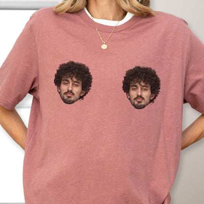 May include: A dusty rose-colored crew neck t-shirt featuring two identical photographic prints of a person with dark curly hair and a beard positioned on the chest area. The shirt has short sleeves and a standard fit, made of a heathered fabric.