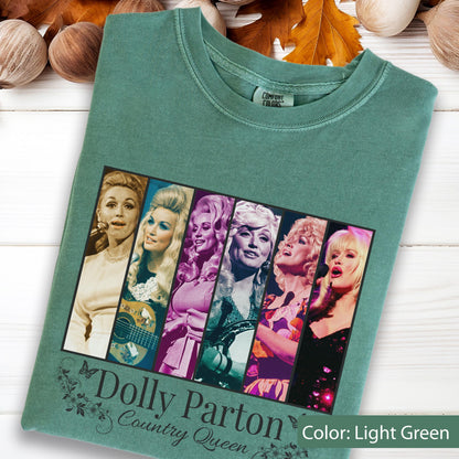 May include: A light green t-shirt featuring a graphic print of six vertical panels displaying various images of Dolly Parton. Below the graphic, the text reads Dolly Parton Country Queen in a decorative font, accompanied by small floral illustrations.