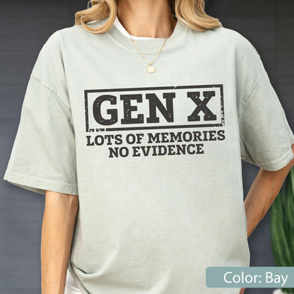 May include: A light sage green short-sleeve t-shirt featuring a black rectangular graphic with the text "GEN X" in a bold, distressed font, followed by the text "LOTS OF MEMORIES NO EVIDENCE" in a smaller, matching black distressed font.