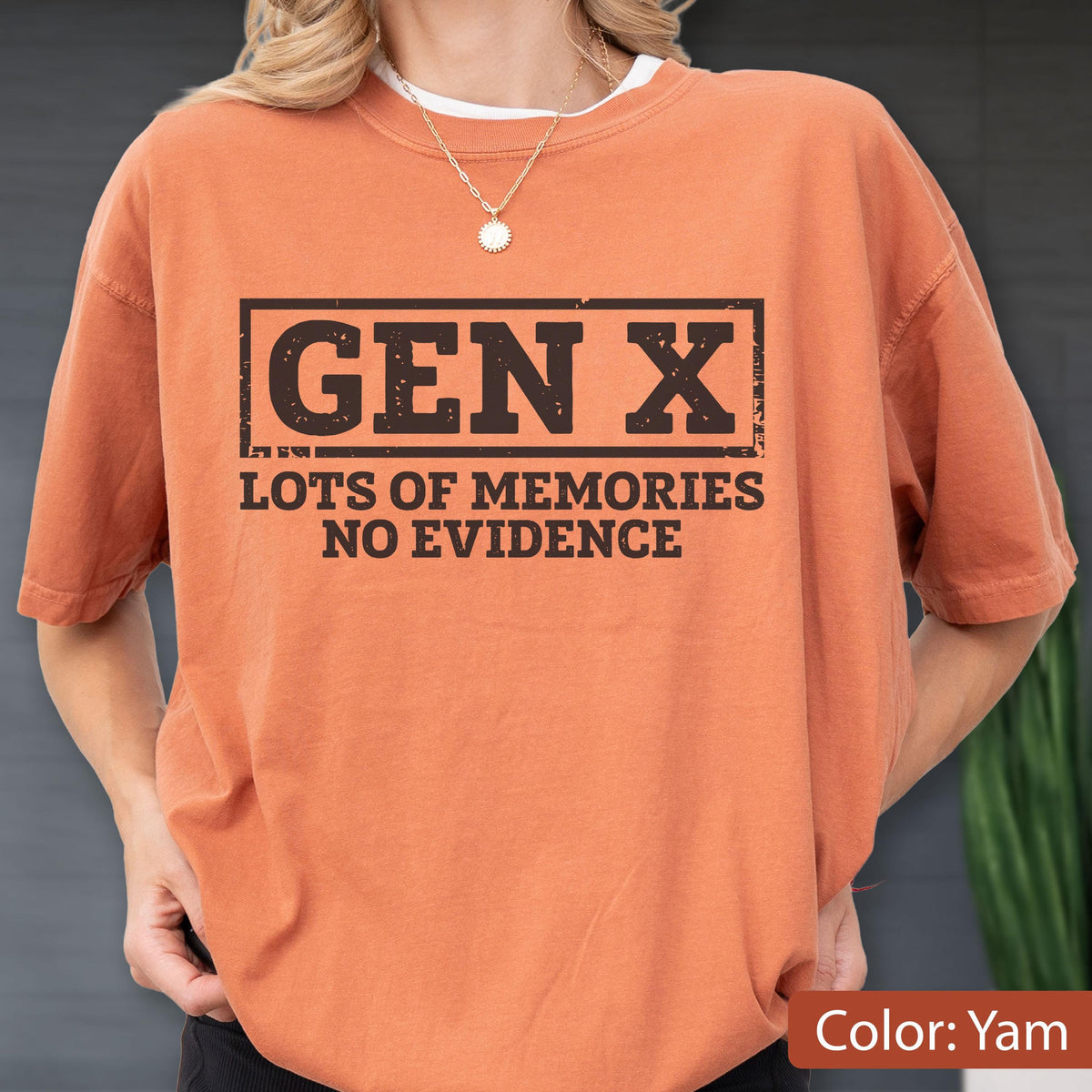 May include: A short-sleeved crew neck t-shirt in a solid yam orange color. The front features a black rectangular graphic with the text GEN X in a bold, distressed font, followed by the text LOTS OF MEMORIES NO EVIDENCE in a matching font.