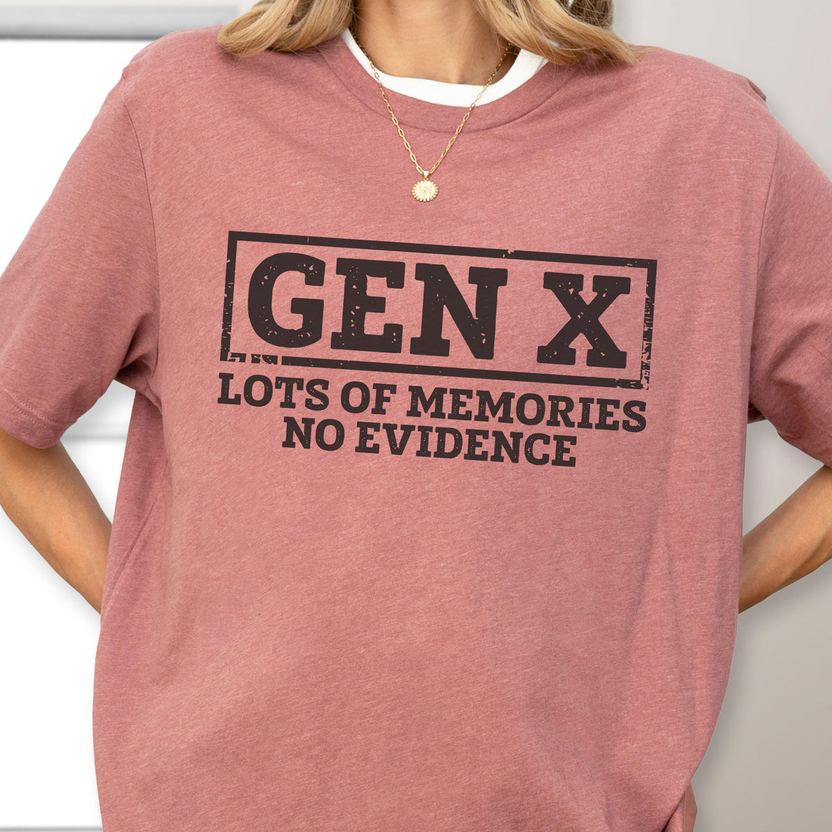 May include: A dusty rose short-sleeve t-shirt featuring a black rectangular graphic with the text GEN X in a bold font, followed by the text LOTS OF MEMORIES NO EVIDENCE in a smaller font. The shirt has a crew neckline and a heathered texture.