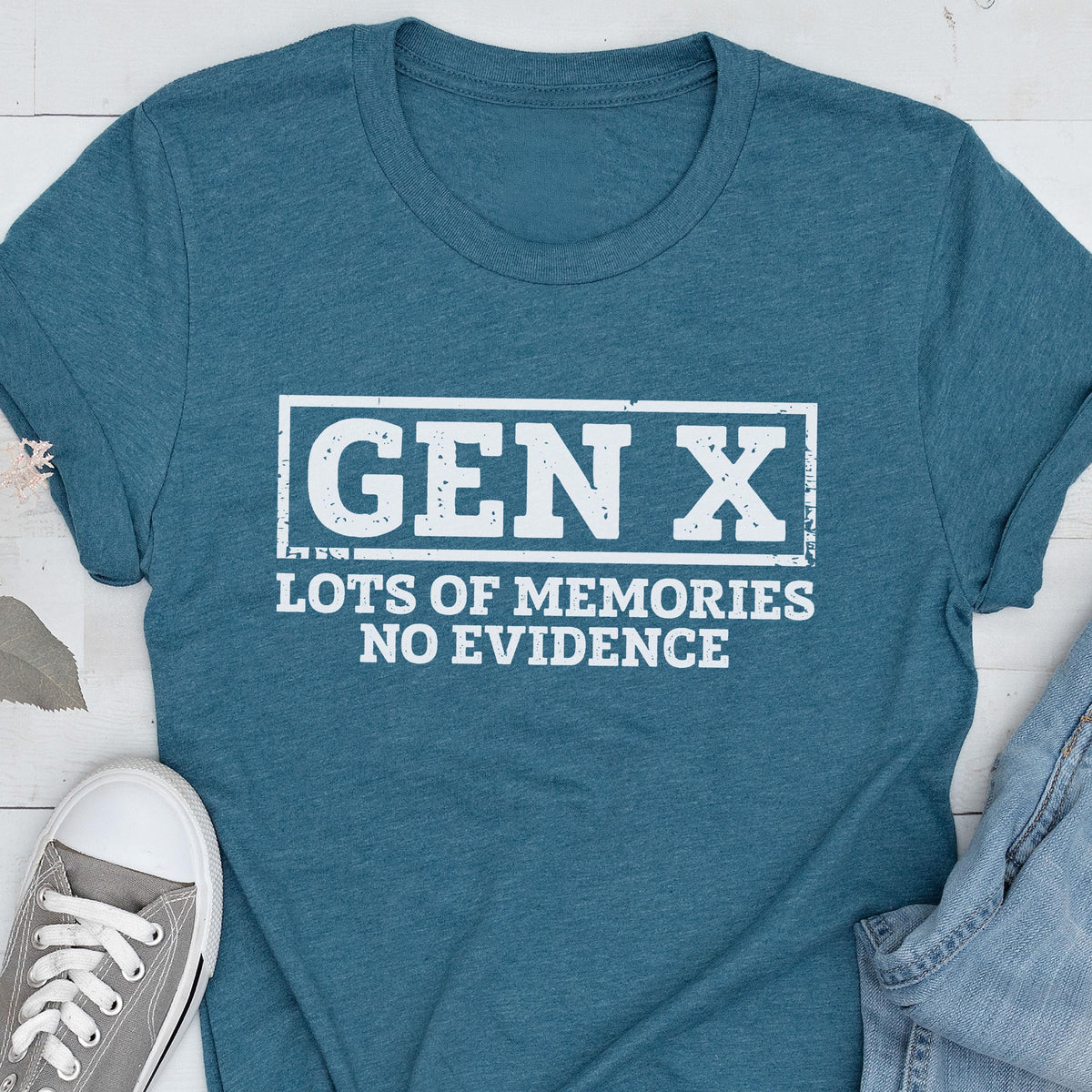 May include: A teal short-sleeved crew neck t-shirt featuring a white rectangular graphic with the distressed text "GEN X" at the top and "LOTS OF MEMORIES NO EVIDENCE" printed in white capital letters underneath the box.