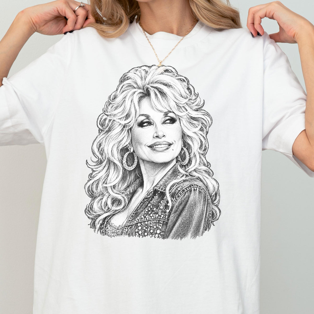 May include: A white t-shirt featuring a detailed black and white pencil-style sketch of a person with voluminous, wavy hair, wearing large hoop earrings and a textured jacket. The illustration is centered on the chest of the garment.