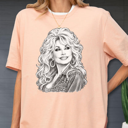 May include: A peach-colored short-sleeve t-shirt featuring a detailed black and white pencil-style sketch graphic of a woman with voluminous wavy hair, wearing large hoop earrings and a textured jacket, centered on the front of the garment.
