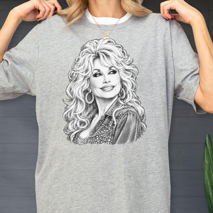 May include: A heather gray short-sleeve t-shirt featuring a detailed black and white pencil-style sketch of a woman with voluminous blonde hair, wearing hoop earrings and a textured jacket, centered on the front of the garment.