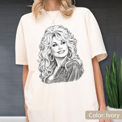 May include: An ivory short-sleeve t-shirt featuring a detailed black and white pencil-style sketch of a woman with voluminous blonde hair, wearing hoop earrings and a textured jacket, centered on the front of the garment.