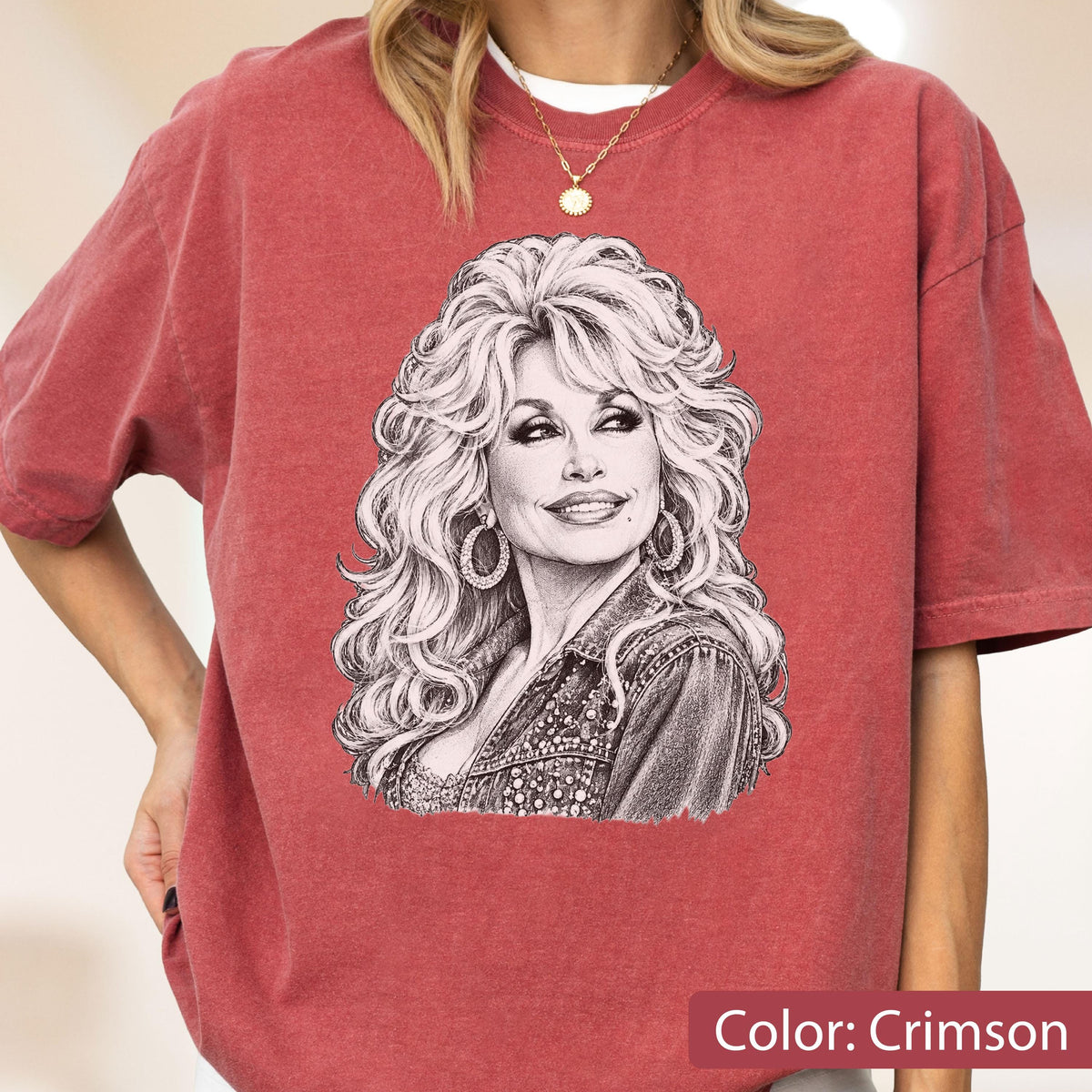 May include: A crimson short-sleeve t-shirt featuring a black and white sketch-style graphic of a person with voluminous blonde hair, hoop earrings, and a collared jacket. The shirt has a crew neckline and a relaxed fit with a vintage-washed texture.