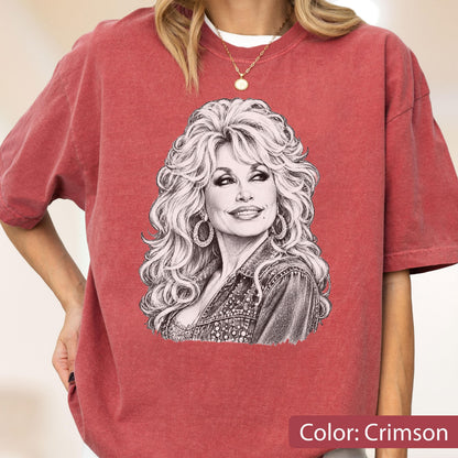 May include: A crimson short-sleeve t-shirt featuring a black and white sketch-style graphic of a person with voluminous blonde hair, hoop earrings, and a collared jacket. The shirt has a crew neckline and a relaxed fit with a vintage-washed texture.