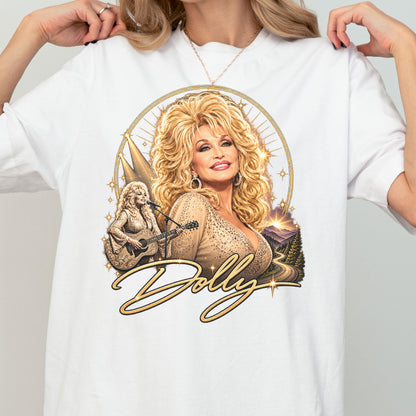 May include: A white t-shirt featuring a graphic print of Dolly Parton with voluminous blonde hair. The design includes a portrait, a smaller image of her playing an acoustic guitar, a mountain landscape, and the script text Dolly in gold.
