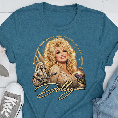 May include: A teal crew neck t-shirt featuring a graphic print of a blonde woman with voluminous hair. The design includes a smaller image of the woman playing an acoustic guitar, a golden circular frame, and the cursive text Dolly in gold.