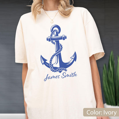 May include: An ivory short-sleeve t-shirt featuring a large blue graphic of a nautical anchor wrapped in a rope. Below the anchor, the text James Smith is printed in a blue script font. The shirt has a crew neckline and a relaxed fit.