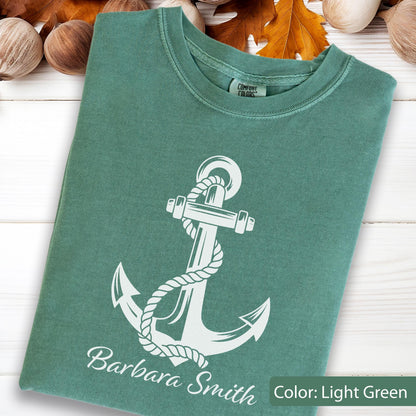 May include: A light green crew neck t-shirt featuring a white graphic of a nautical anchor wrapped in rope. The text "Barbara Smith" is printed in white below the anchor. The shirt has a Comfort Colors brand label inside the neckline.