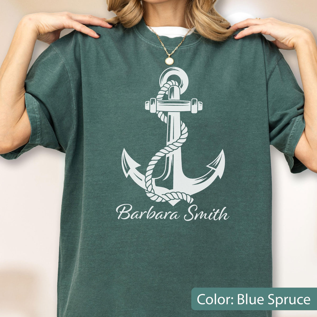 May include: A dark blue-green crew neck t-shirt featuring a large white graphic of a nautical anchor wrapped in a rope. Below the anchor, the name Barbara Smith is printed in a white script font. The shirt has short sleeves and a relaxed fit.