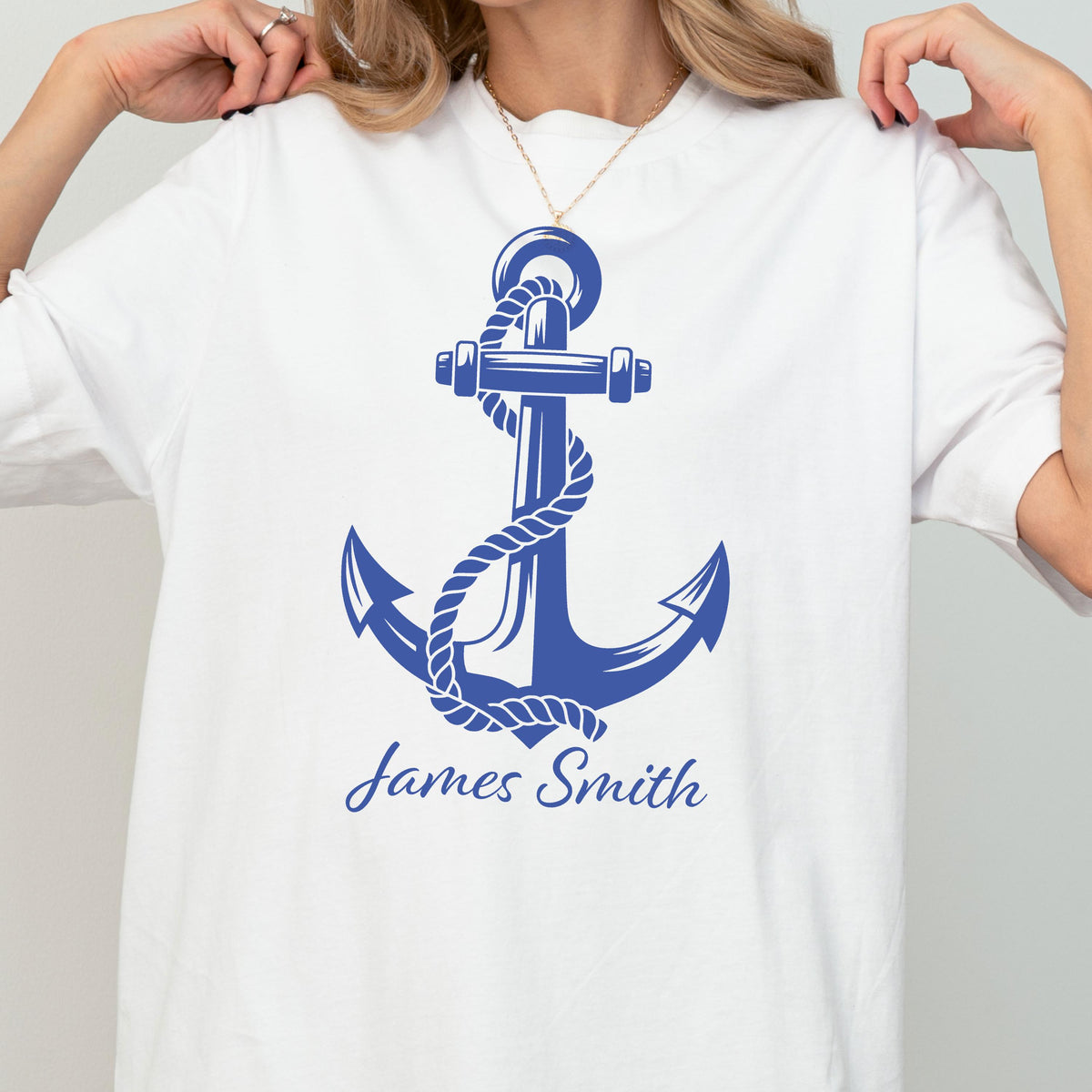 May include: A white short-sleeved t-shirt featuring a large blue graphic of a nautical anchor wrapped in a rope. Below the anchor, the name James Smith is printed in a blue script font. The design is centered on the front of the garment.