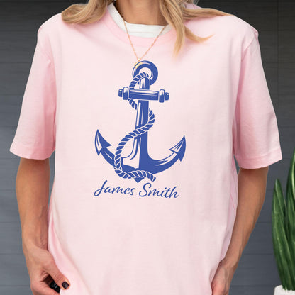 May include: A light pink short-sleeved t-shirt featuring a large dark blue graphic of a nautical anchor wrapped in a rope. Below the anchor, the name James Smith is printed in a dark blue cursive script font on the front of the garment.