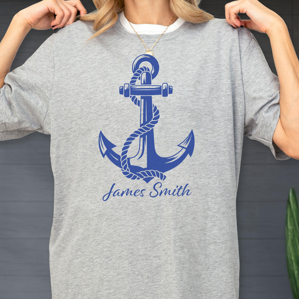May include: A heather gray short-sleeve t-shirt featuring a large blue graphic of a nautical anchor wrapped in rope. Below the anchor, the name James Smith is printed in a blue script font. The shirt has a crew neckline and a relaxed fit.
