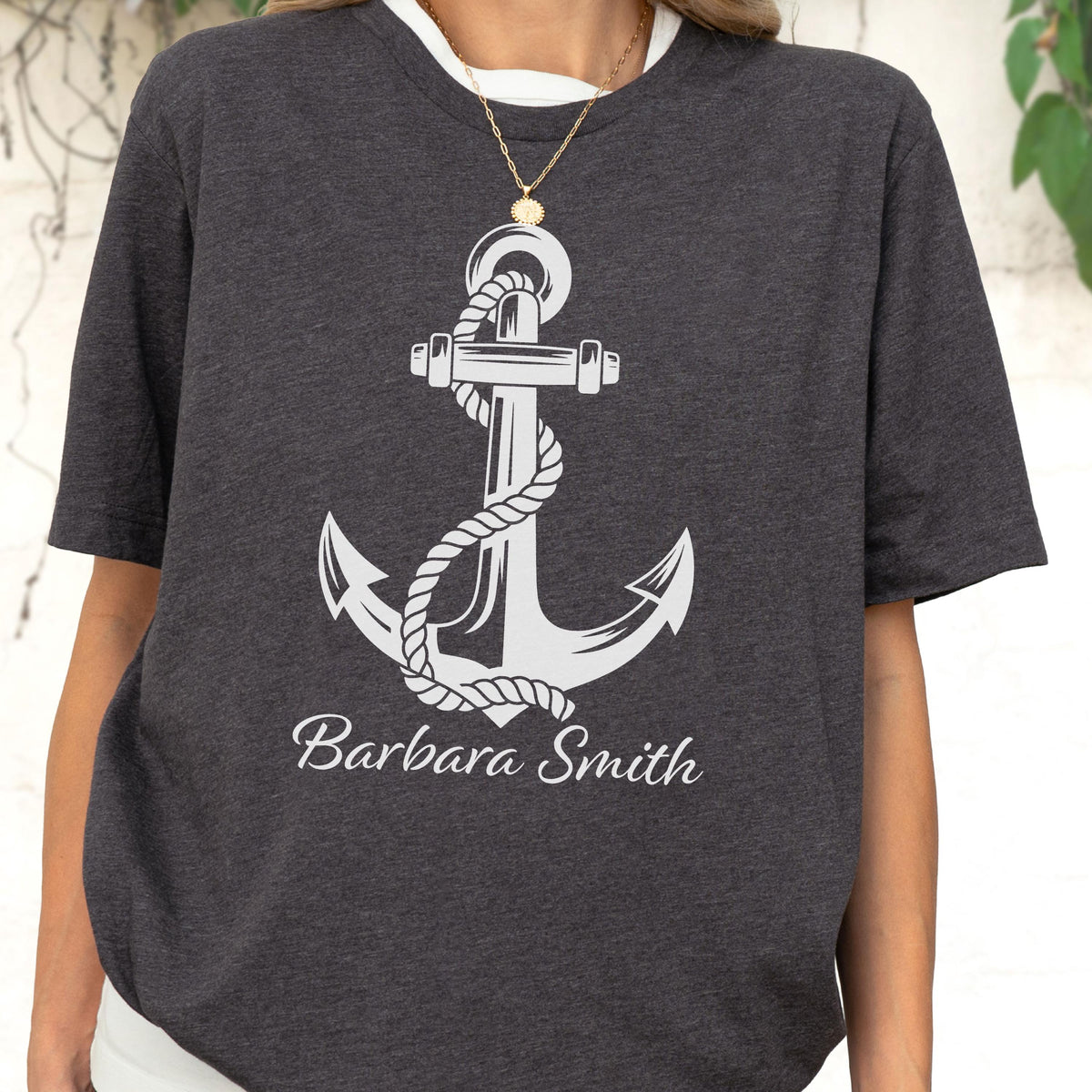 May include: A dark charcoal gray short-sleeve t-shirt featuring a large white graphic of a nautical anchor wrapped in a rope. Below the anchor, the name Barbara Smith is printed in a white cursive script font across the chest area.