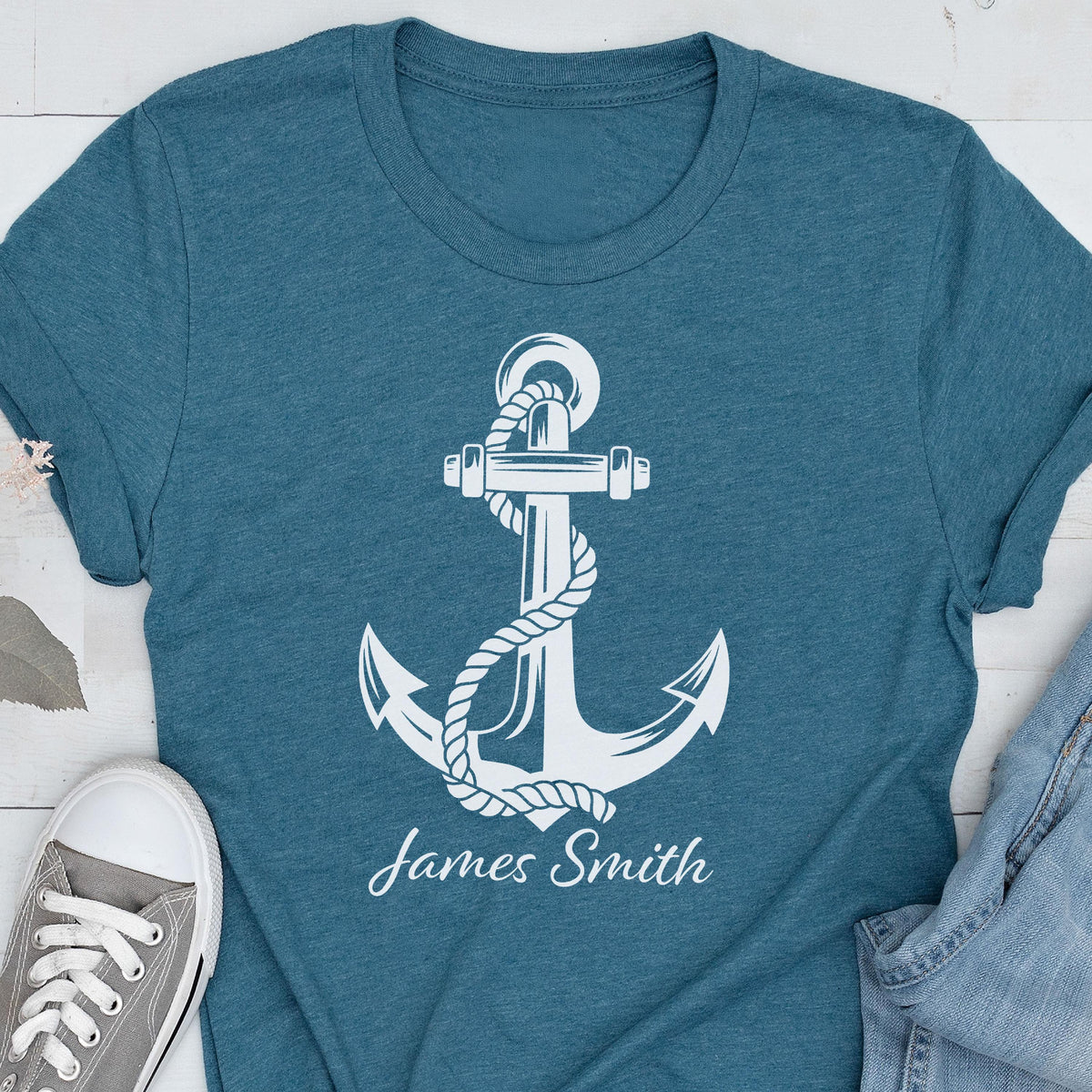 May include: A heathered teal short-sleeve t-shirt featuring a large white graphic of a nautical anchor wrapped in rope. Below the anchor, the name James Smith is printed in a white script font. The shirt has a crew neckline and a standard fit.