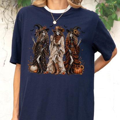 May include: A dark navy blue t-shirt featuring a graphic print of three skeletons dressed in western-style clothing, including hats, dresses, and boots. The skeletons are surrounded by sunflowers, pumpkins, and small bats on a dark background.