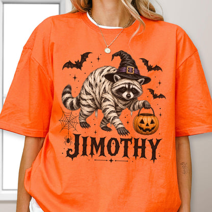 May include: An orange t-shirt featuring a graphic of a raccoon wrapped in mummy bandages, wearing a black witch hat, and holding a jack-o'-lantern. The design includes bats, a spider web, and the name JIMOTHY printed in black lettering.