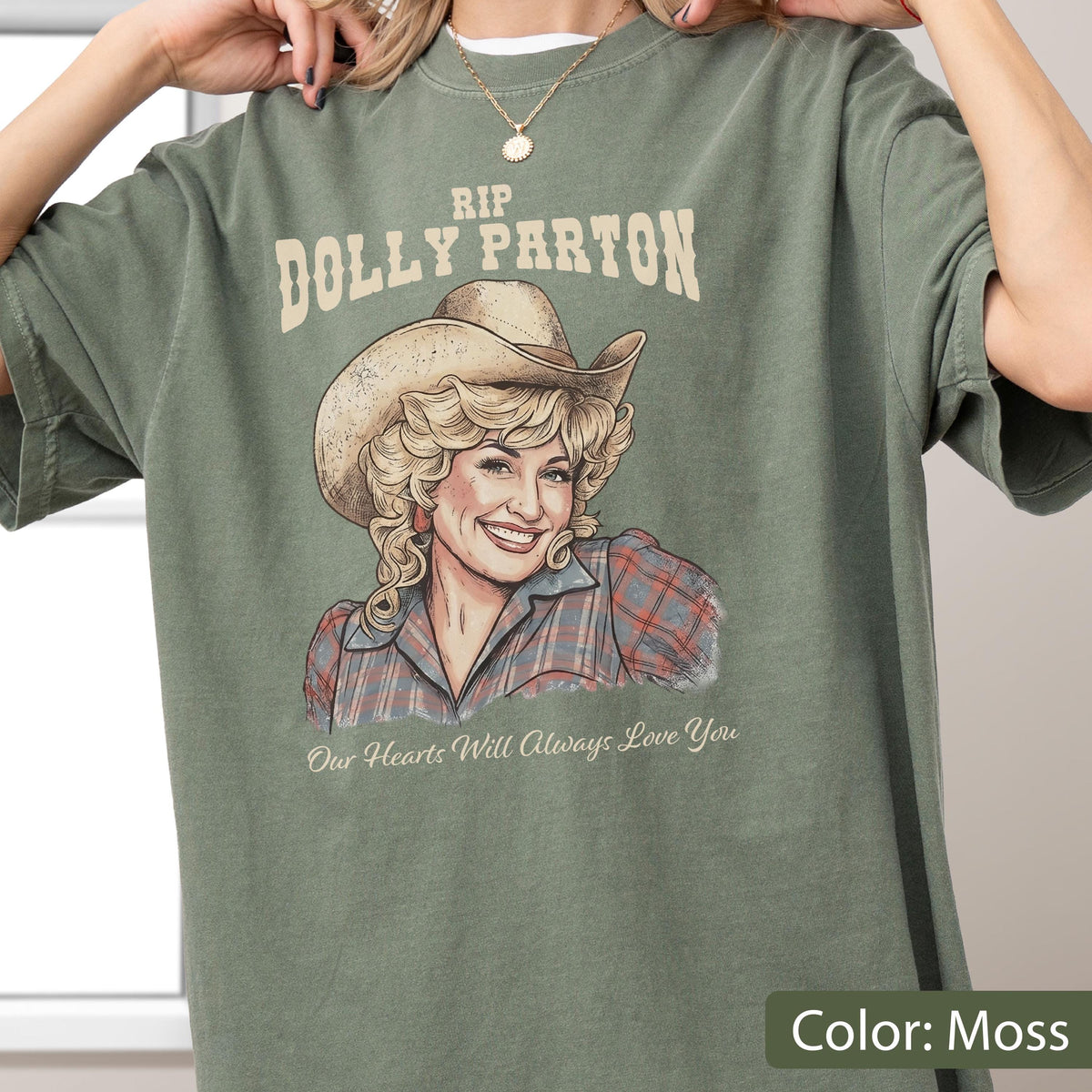 May include: A moss green t-shirt featuring a graphic illustration of Dolly Parton wearing a cowboy hat and a plaid shirt. The text reads RIP DOLLY PARTON at the top and Our Hearts Will Always Love You at the bottom in a cream-colored font.