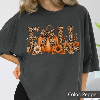 May include: A charcoal gray t-shirt featuring a graphic print of the word FALL. The letters are filled with a leopard print pattern. An orange pumpkin with a leopard print bow sits in the center, surrounded by sunflowers and autumn leaves.