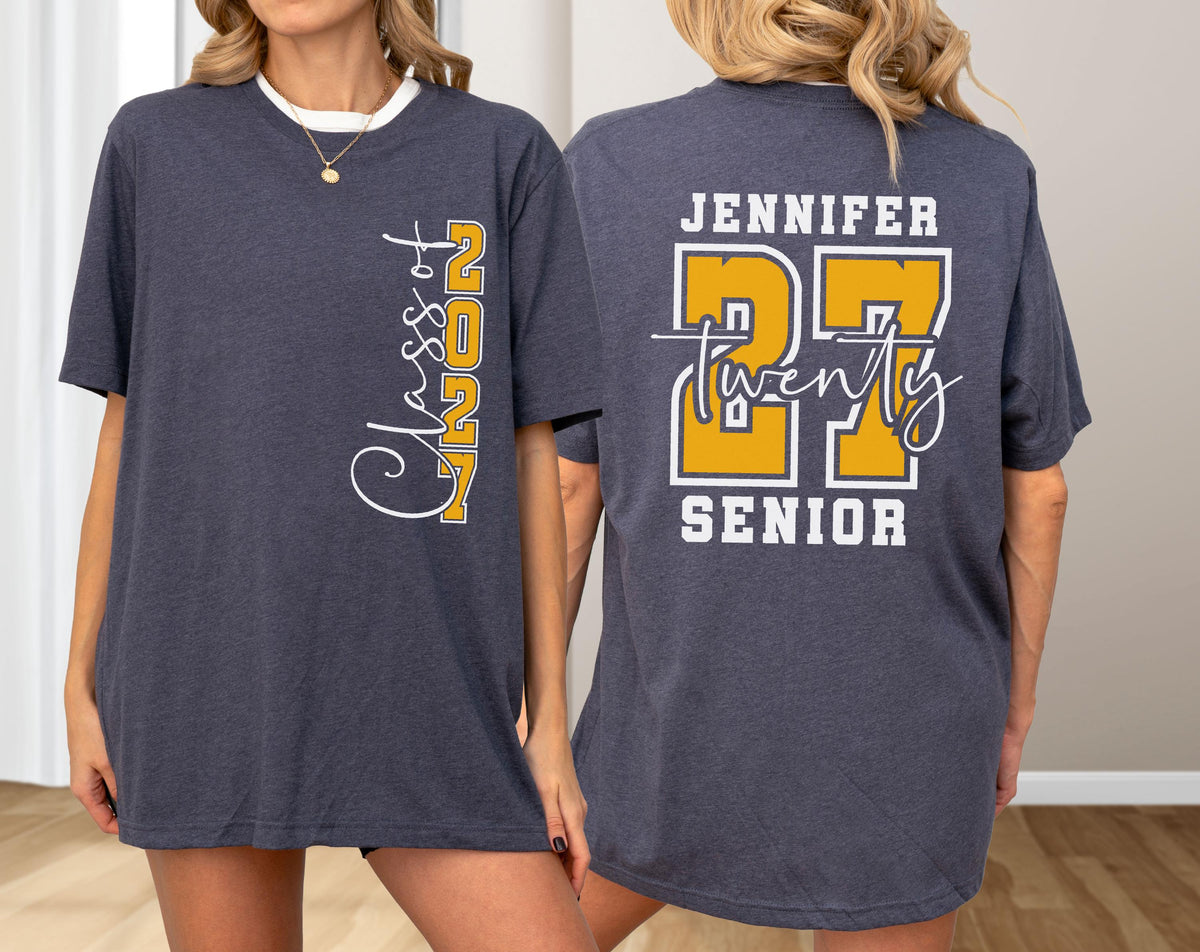 May include: A dark heather gray t-shirt featuring a vertical white and yellow graphic on the front that reads Class of 2027. The back displays the name Jennifer, the large yellow number 27, the word twenty in script, and the word SENIOR in white.
