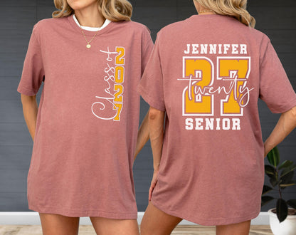May include: A dusty rose t-shirt featuring a front graphic with the vertical text Class of 2027 in white and yellow. The back displays the name Jennifer, the number 27 in large yellow block letters with white outlines, and the word twenty in script.