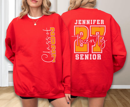 May include: A bright red crewneck sweatshirt featuring white and orange graphic text. The front displays vertical text reading Class of 2027. The back features the name Jennifer, the number 27 in large orange font, the word twenty in script, and Senior.