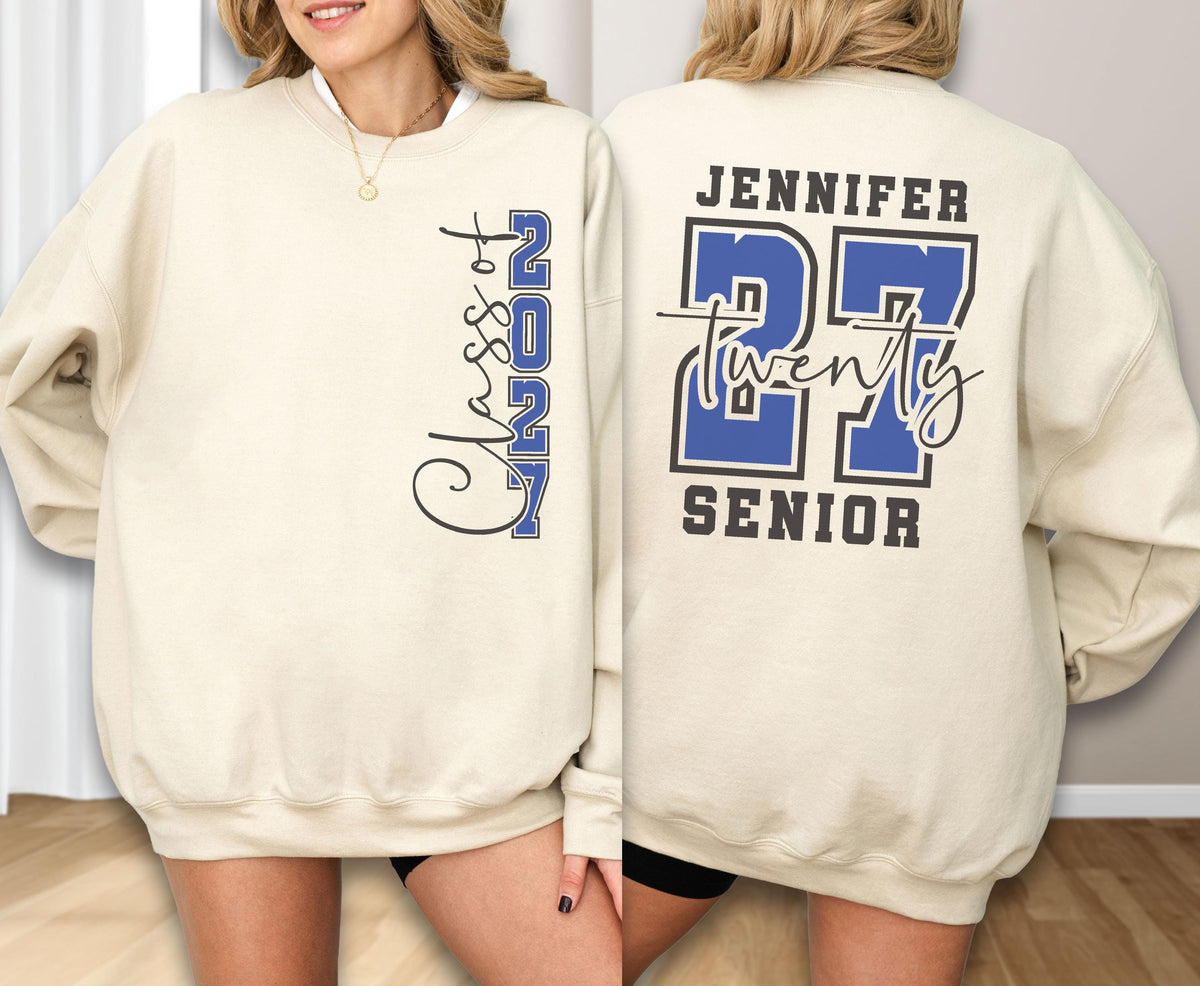 May include: A beige crewneck sweatshirt featuring a blue and black graphic design. The front displays vertical text reading Class of 2027. The back features the name Jennifer, the number 27, the word twenty in script, and the word SENIOR in block letters.