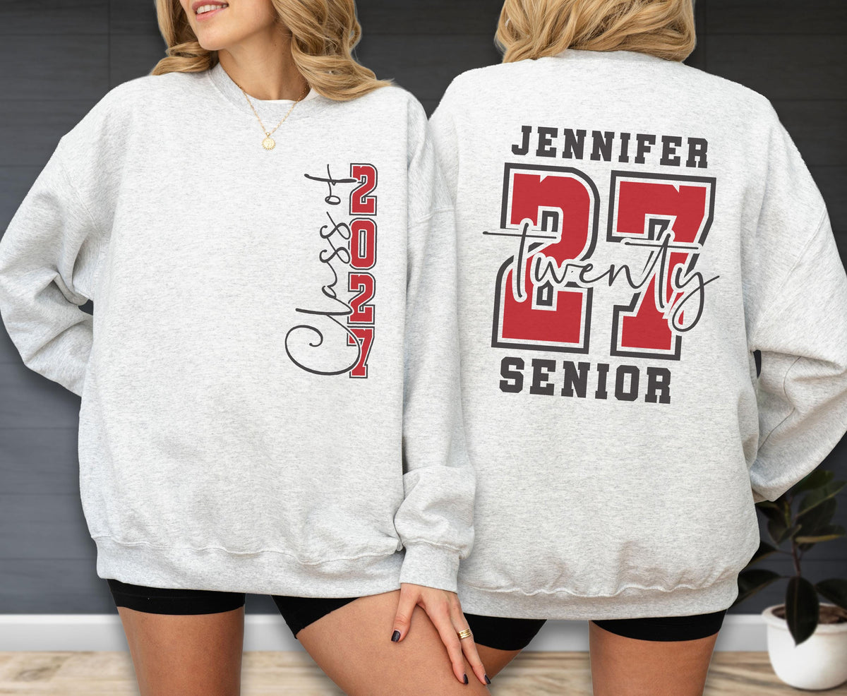May include: A light gray crewneck sweatshirt featuring a vertical graphic on the front that reads Class of 2027 in black and red. The back displays the name Jennifer above the large red number 27, the word twenty in script, and the word SENIOR.