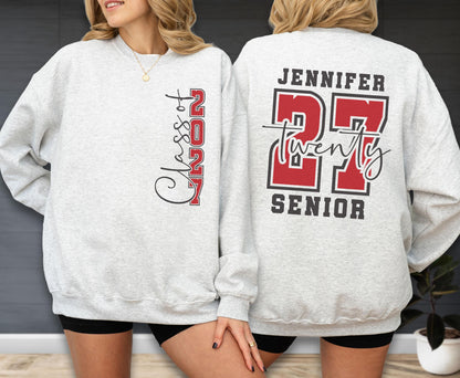 May include: A light gray crewneck sweatshirt featuring a vertical graphic on the front that reads Class of 2027 in black and red. The back displays the name Jennifer above the large red number 27, the word twenty in script, and the word SENIOR.