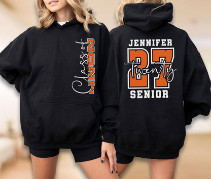 May include: A black hooded sweatshirt featuring white and orange text. The front displays "Class of 2027" vertically. The back shows the name "JENNIFER" above a large orange "27" with the word "twenty" in white script and "SENIOR" printed below.