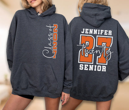 May include: A dark charcoal gray hooded sweatshirt featuring white and orange text. The front displays "Class of 2027" vertically. The back shows the name "JENNIFER" above large orange "27" numerals, the word "twenty" in script, and "SENIOR" at the bottom.