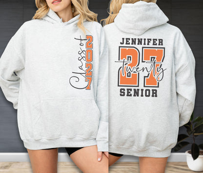 May include: A light gray hooded sweatshirt featuring a front graphic with the vertical text Class of 2027 in black and orange. The back displays the name Jennifer above the large orange number 27, the word twenty in script, and the word Senior.