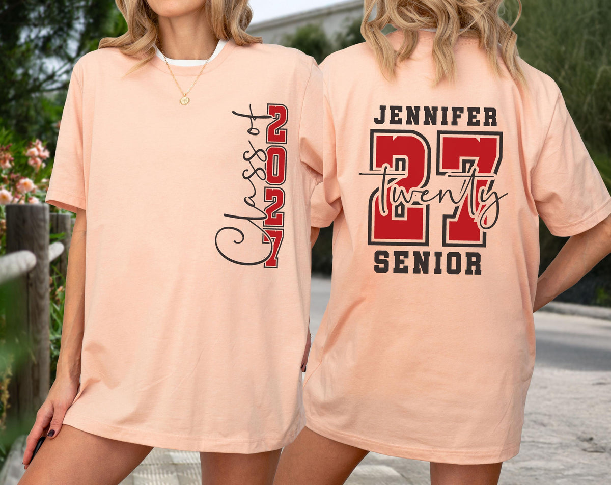 May include: A peach-colored t-shirt featuring a vertical black and red graphic on the front that reads Class of 2027. The back displays the name Jennifer above the number 27 in red with black outlines, the word twenty, and the word Senior.