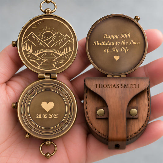 A hand holding a personalized compass with a wooden case and a message engraved on it.