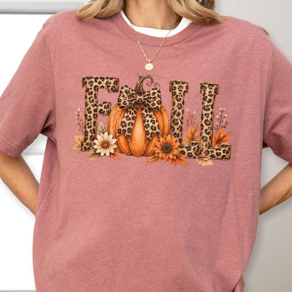 May include: A mauve short-sleeved t-shirt featuring a graphic print of the word FALL in a leopard print pattern. The letter A is replaced by an orange pumpkin with a leopard print bow, surrounded by sunflowers and autumn leaves.