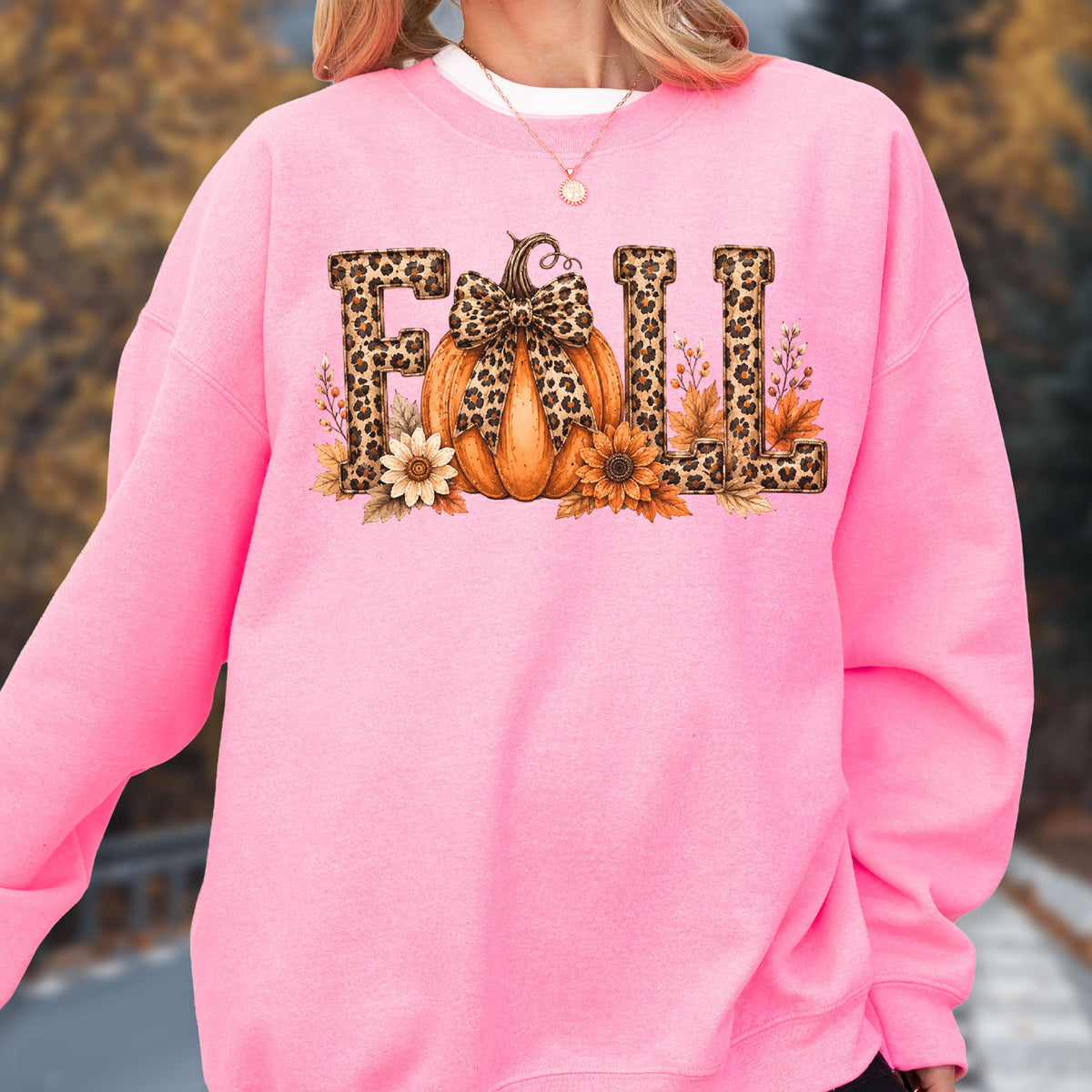 May include: A bright pink long-sleeve sweatshirt featuring the word FALL in large block letters with a leopard print pattern. The letter A is replaced by an orange pumpkin with a leopard print bow, surrounded by sunflowers and autumn leaves.