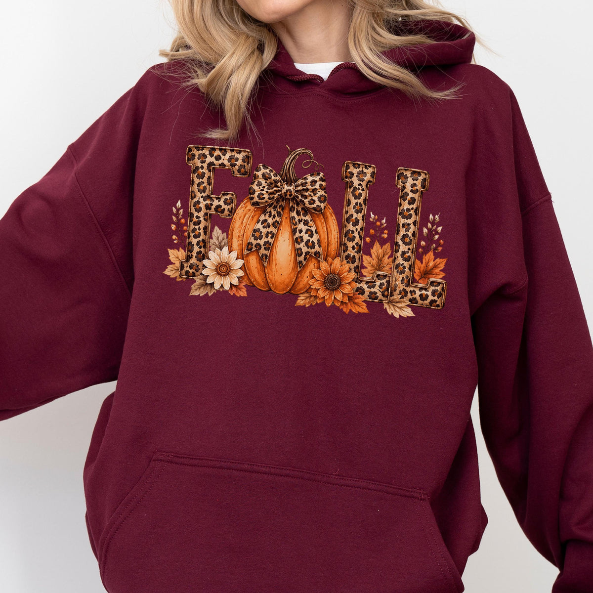 May include: A maroon hooded sweatshirt featuring a graphic print on the chest. The design displays the word FALL in block letters with a leopard print pattern. An orange pumpkin with a leopard print bow sits between the letters, surrounded by sunflowers and autumn leaves.