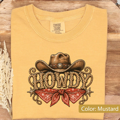 May include: A mustard yellow t-shirt featuring a graphic print of a brown cowboy hat resting above the word HOWDY, which is stylized to look like coiled rope. Below the text is a red bandana with a white pattern and two small silver stars.