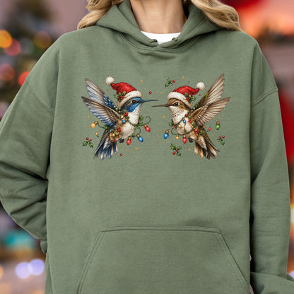 May include: An olive green hooded sweatshirt featuring a graphic print of two hummingbirds wearing red and white Santa hats. The birds are surrounded by colorful Christmas light bulbs and green holly leaves with red berries on the chest area.